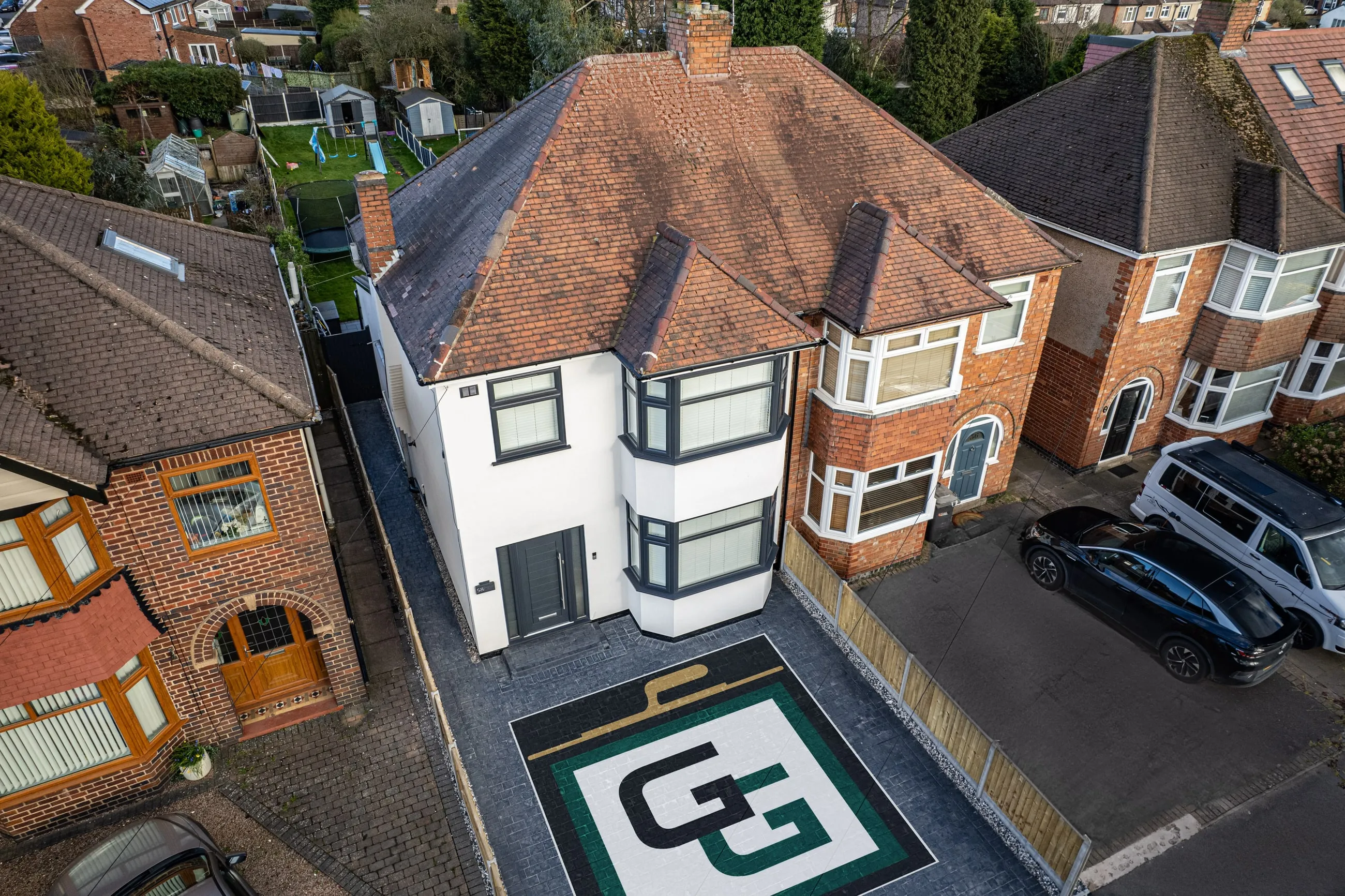 An aerial view of a house finished in brilliant white monocouche render, with the G Green GG monogram laid into the driveway below it.