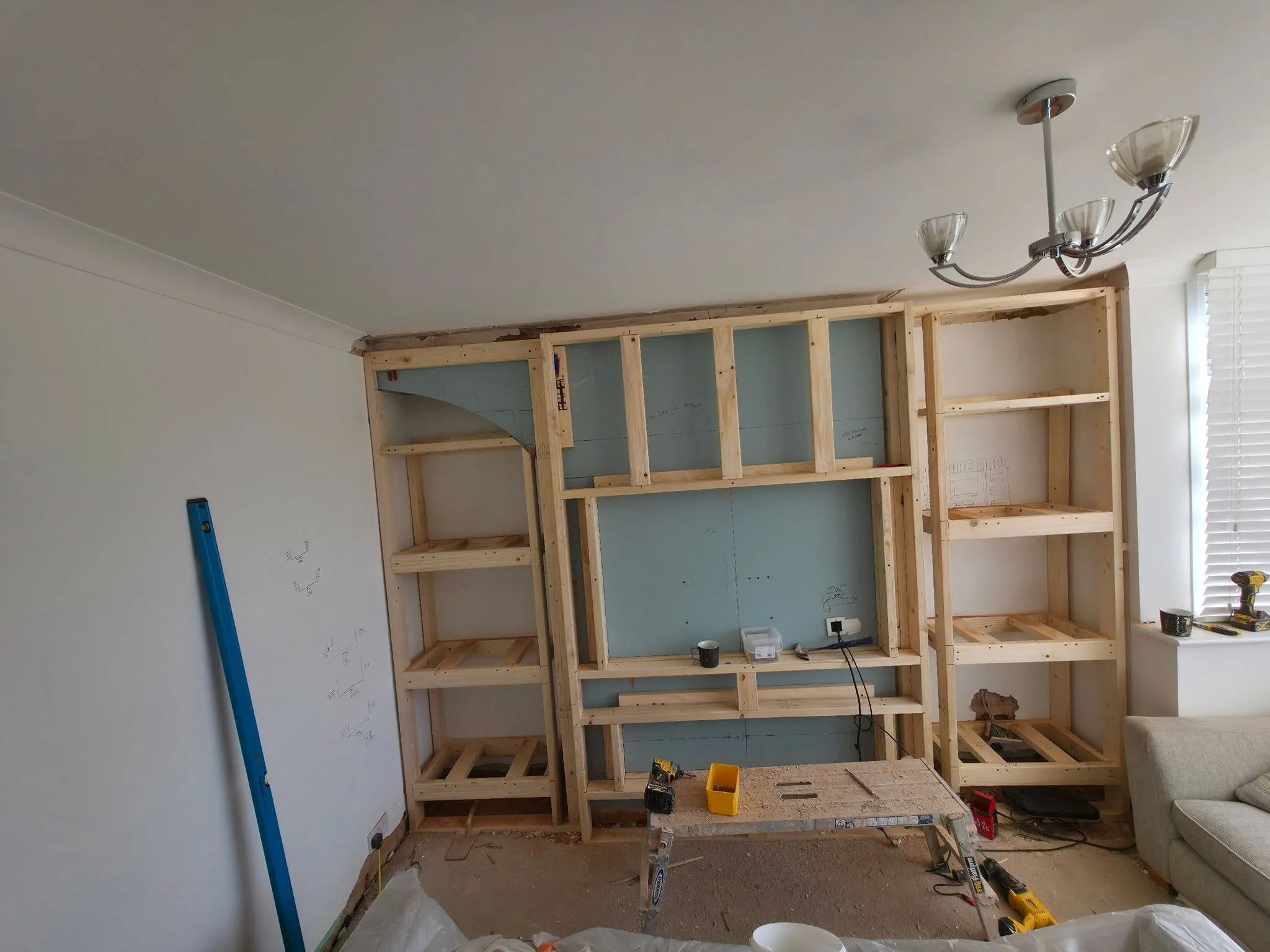 A media wall mid-build as a bare timber stud frame, showing the shelving alcoves and central recess taking shape.