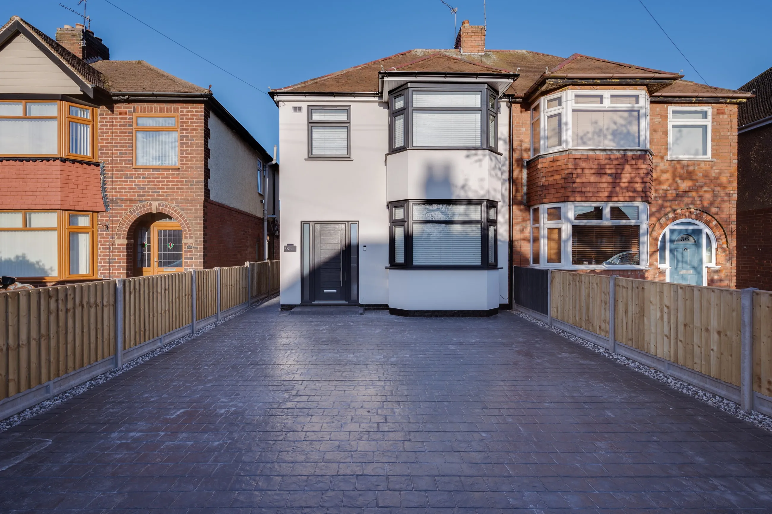 The finished white monocouche-rendered house viewed from the driveway, sitting between two unrendered red-brick neighbours.