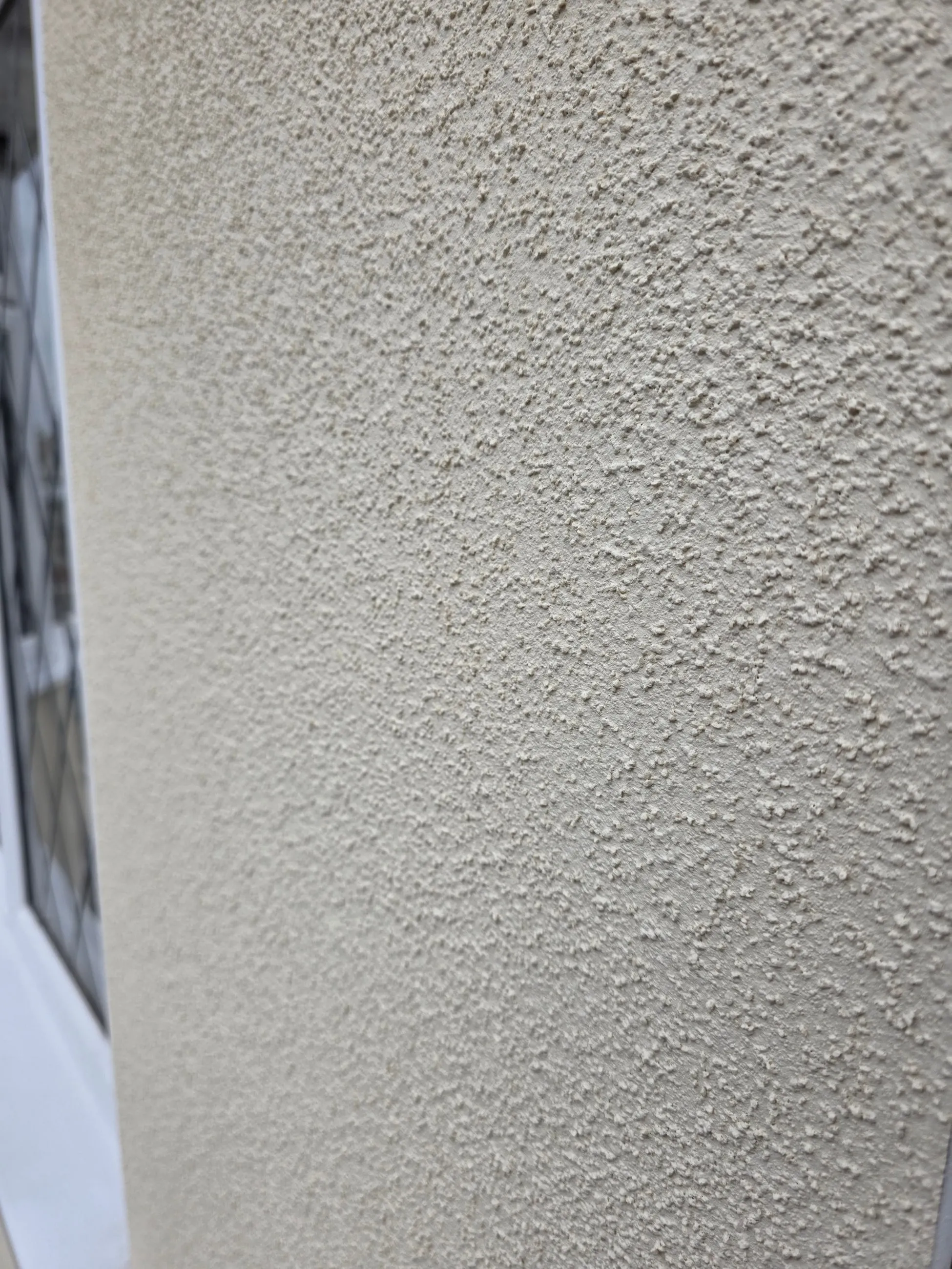 An extreme close view of a finished render surface, showing the fine even grain of the texture across a wall and around its corner.