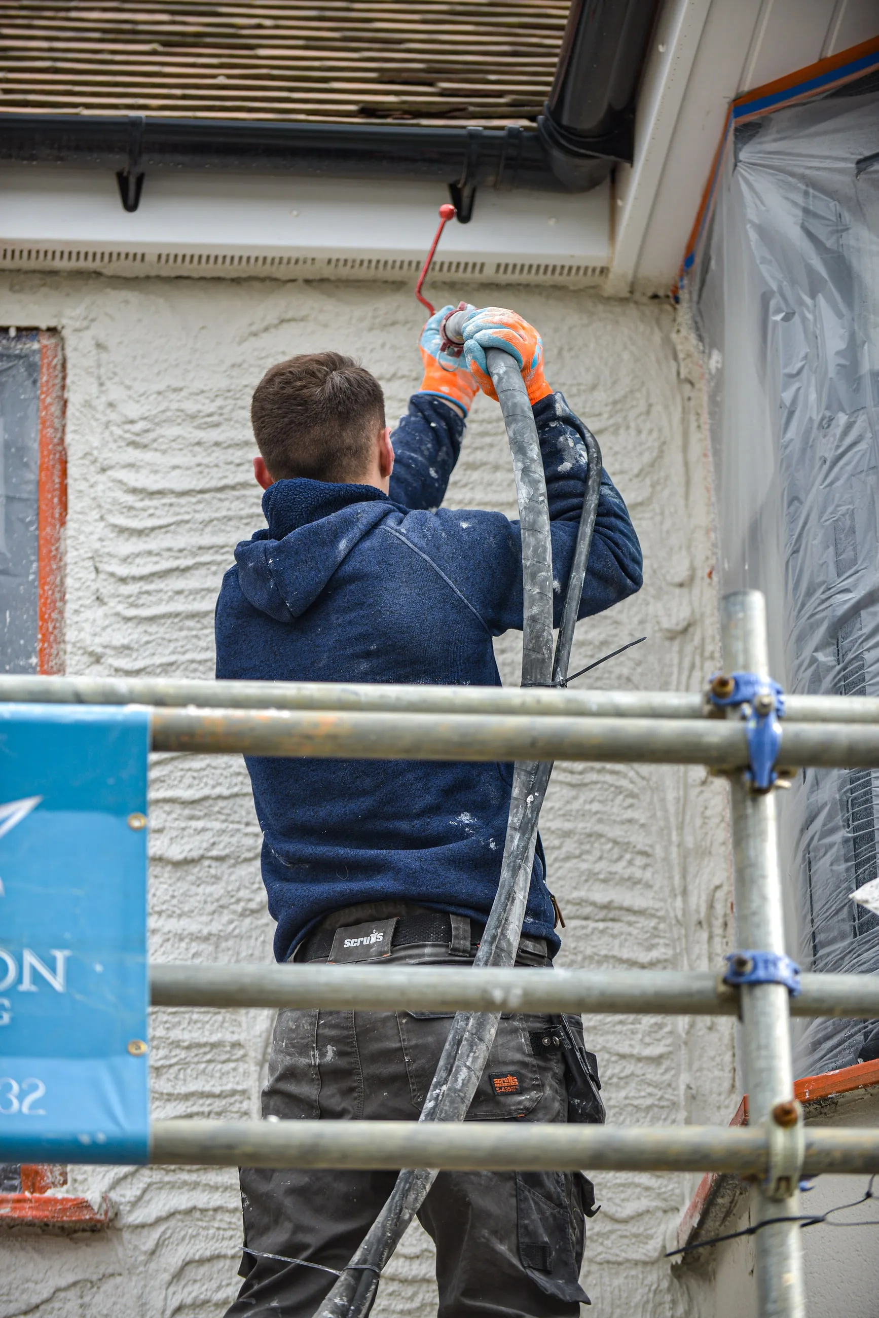 A renderer on a scaffold spraying an upper elevation, the finished lower section visible below.