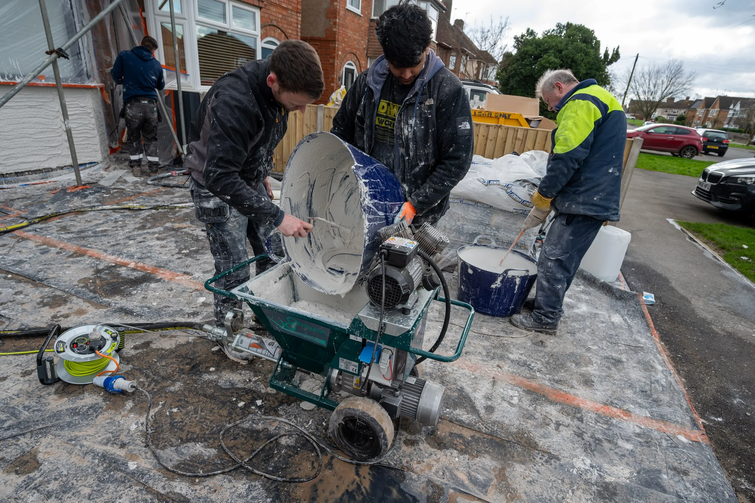 Three of the team working a render mixing pump on the road outside a job, bags and buckets around them.